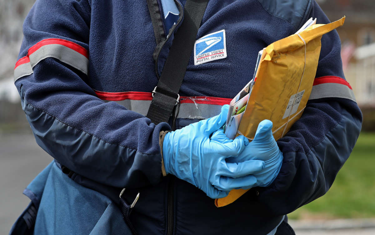 A USPS postal worker wears protective gloves while making deliveries in Cambridge, Massachussetts, during the COVID-19 pandemic on April 8, 2020.