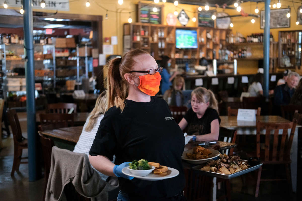 A waitress wearing rubber gloves and a mask is seen bringing out food for patrons at Puckett's Grocery & Restaurant on April 27, 2020, in Franklin, Tennessee. Tennessee is one of the first states to reopen restaurants after the onset of COVID-19.