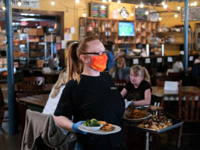 A waitress wearing rubber gloves and a mask is seen bringing out food for patrons at Puckett's Grocery & Restaurant on April 27, 2020, in Franklin, Tennessee. Tennessee is one of the first states to reopen restaurants after the onset of COVID-19.