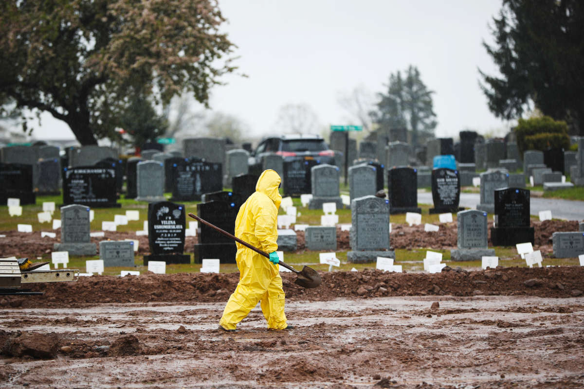 A worker carries a shovel through a graveyard