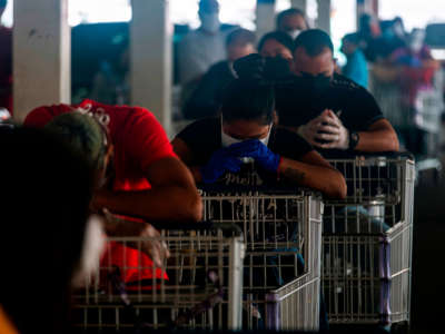 People wear face masks to protect against the coronavirus keep their distance as they queue at a supermarket during a mandatory confinement to counter the new coronavirus in Carolina, Puerto Rico, on April 7, 2020.