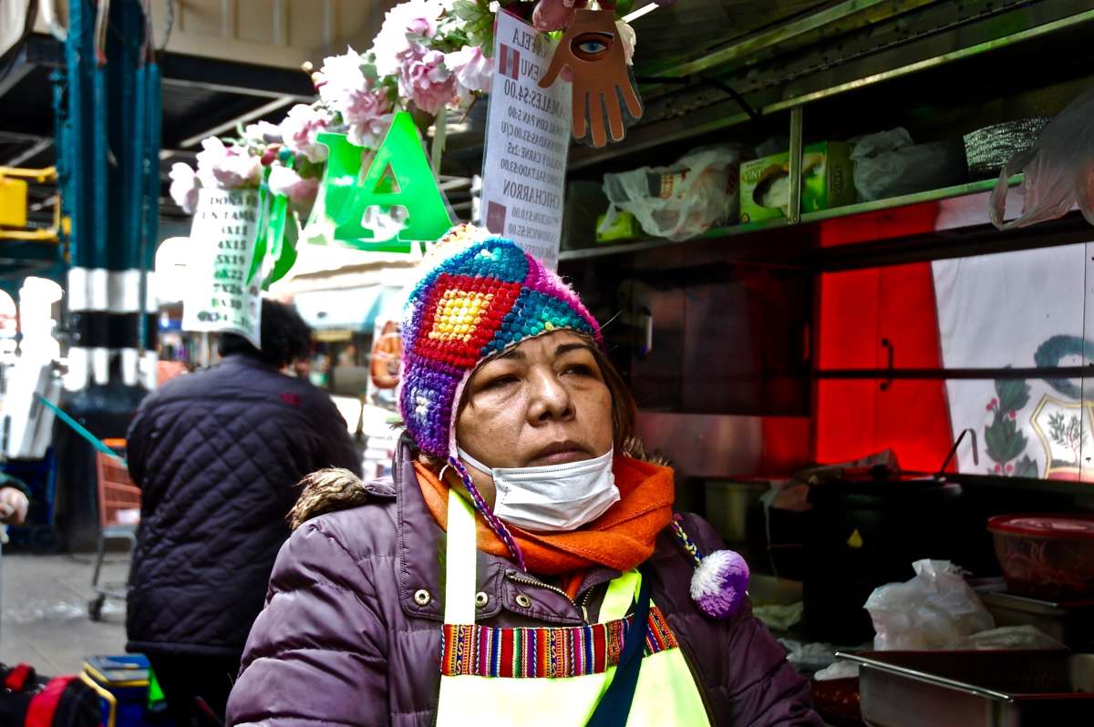 A woman in a face mask stands near a booth in an outdoor market