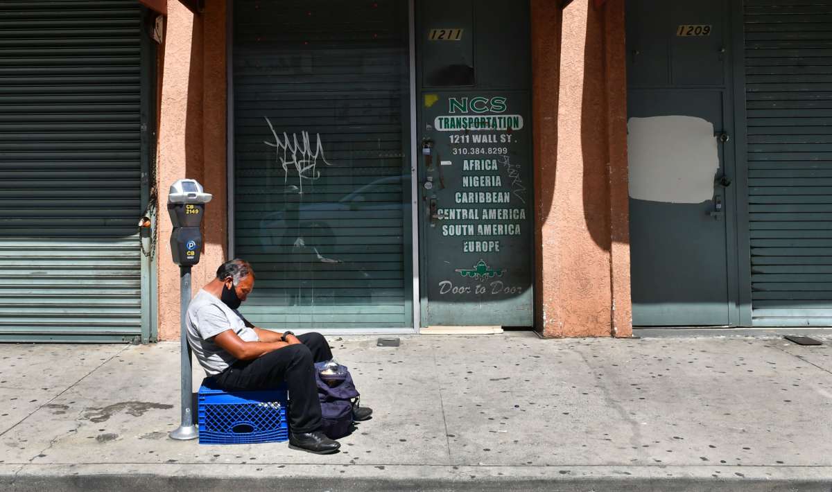A man sits on a turned-over milk crate in front of shuttered businesses