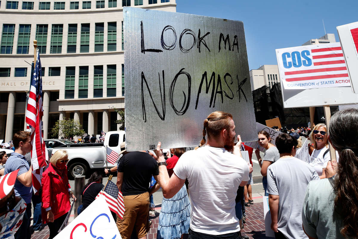 A man holds a sign reading "Look Ma No Mask" at a protest