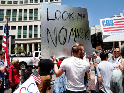 A man holds a sign reading "Look Ma No Mask" at a protest