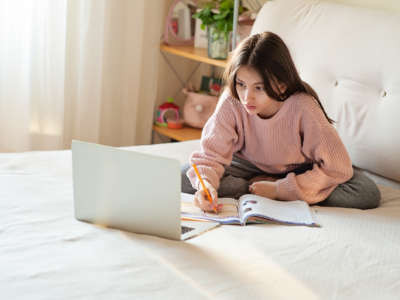 A student writes in a notebook while looking at her laptop