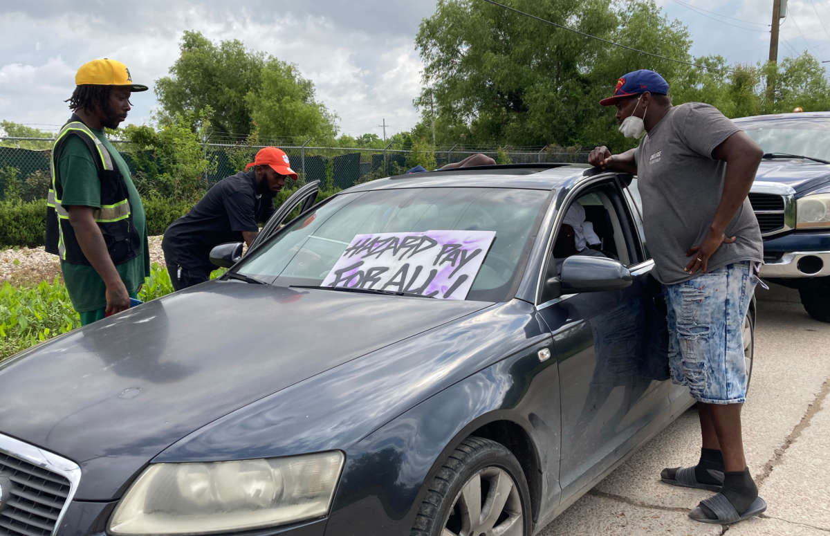 Rahman Brooks and other striking sanitation workers gather around a car at a picket line in New Orleans. The strikers are demanding higher wages and better working conditions from a private contractor and city officials.