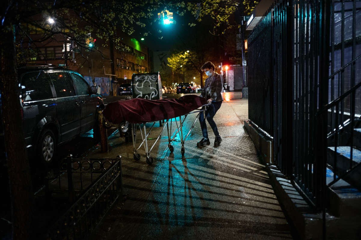 A funeral home director wheels a body out of a new york brownstone lit by streetlights