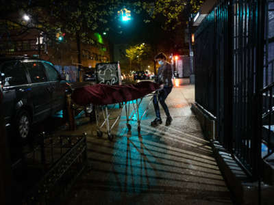 A funeral home director wheels a body out of a new york brownstone lit by streetlights