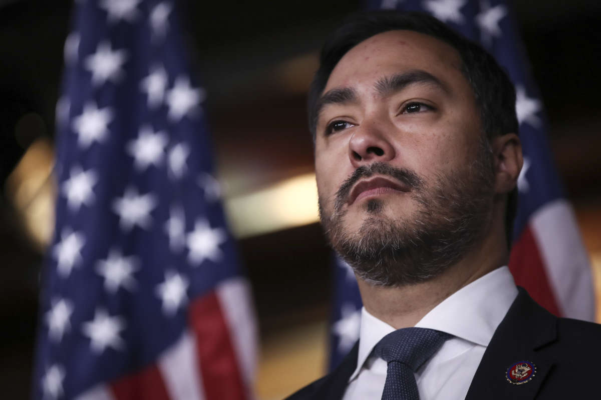 Rep. Joaquin Castro looks out at his audience as U.S. flags hang in the background