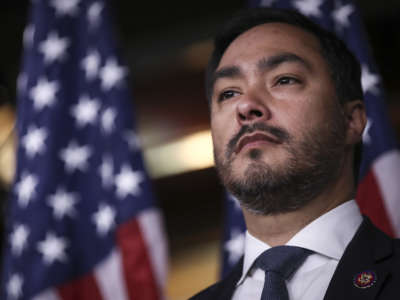 Rep. Joaquin Castro looks out at his audience as U.S. flags hang in the background