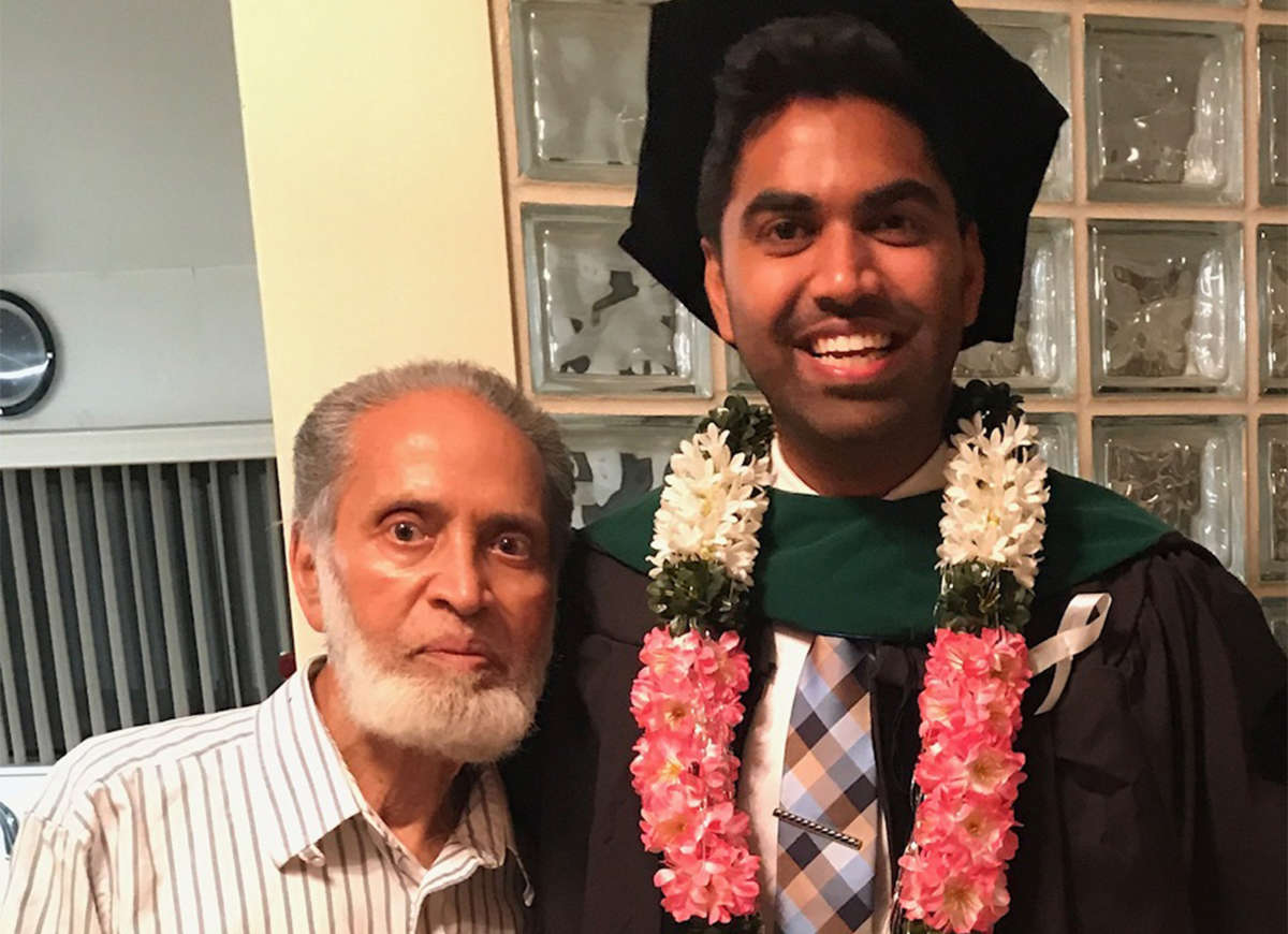 An older man stands beside his grandson, who is dressed for his graduation