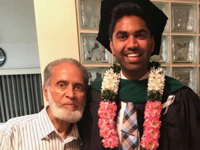 An older man stands beside his grandson, who is dressed for his graduation