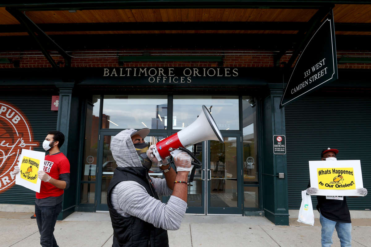 A man in a mask speaks into a megaphone as others display signs while safely distanced behind him