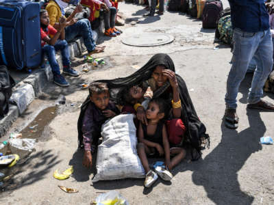 A woman covers her children with a shawl to protect them from the sun as she waits with other migrant workers and families to get registered for a train going to their native places after the goverment eased a nationwide lockdown imposed as a preventive measure against the COVID-19 coronavirus, in New Delhi, India, on May 20, 2020.