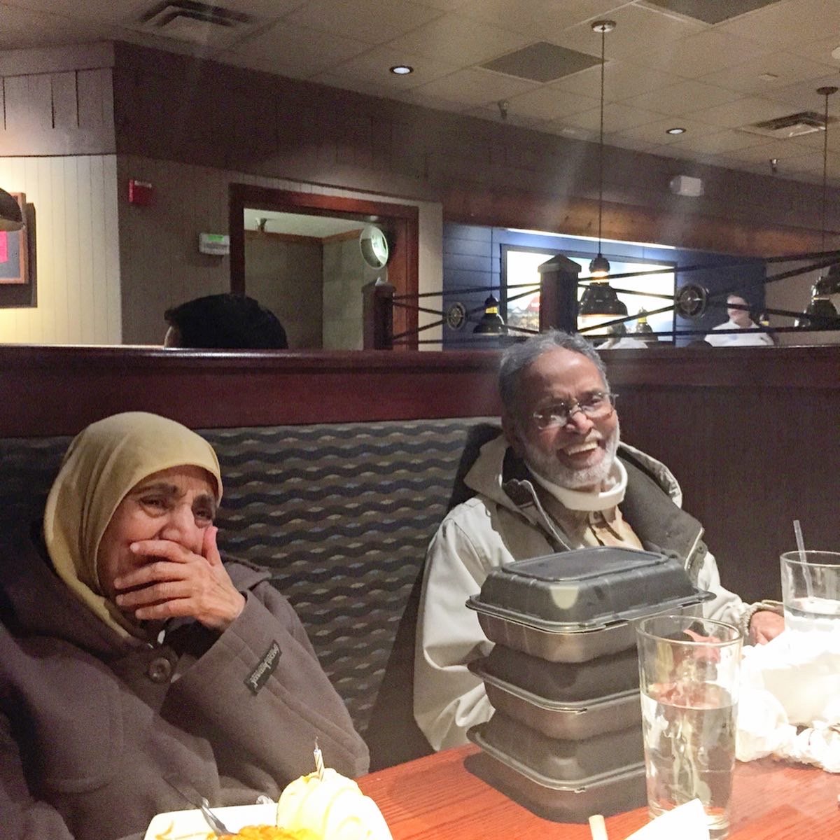 A woman in a hijab covers her mouth while laughing with an older gentleman sitting beside her