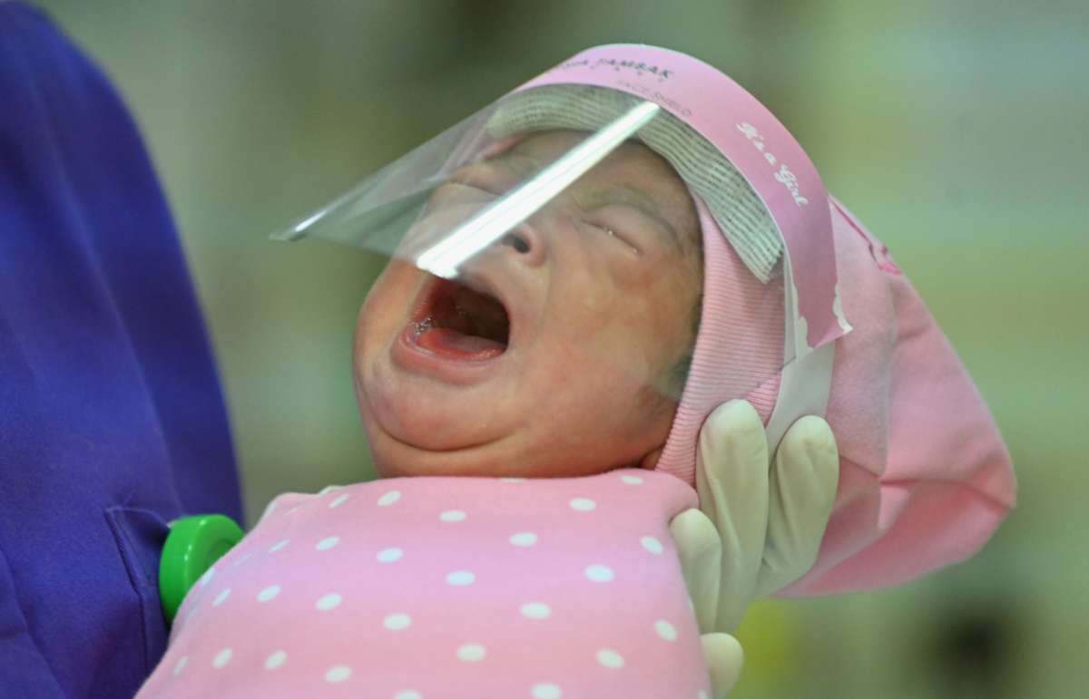 A nurse holds a newborn baby, seen wearing a face shield as a protective measure amid the COVID-19 coronavirus pandemic.