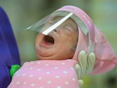 A nurse holds a newborn baby, seen wearing a face shield as a protective measure amid the COVID-19 coronavirus pandemic.