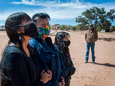 Two Navajo women and a girl stand next to eachother with facemasks on as an Elder, also in a facemask, looks on