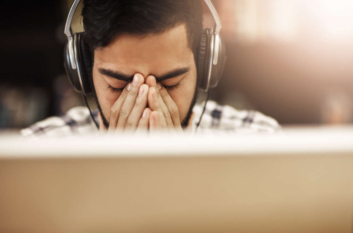 A college-aged studnt massages the bridge of his nose in exhaustion as he sits in front of a laptop