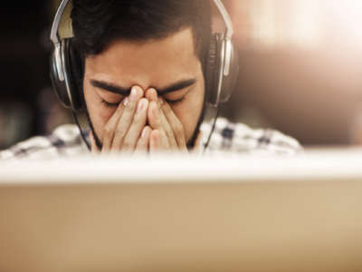 A college-aged studnt massages the bridge of his nose in exhaustion as he sits in front of a laptop