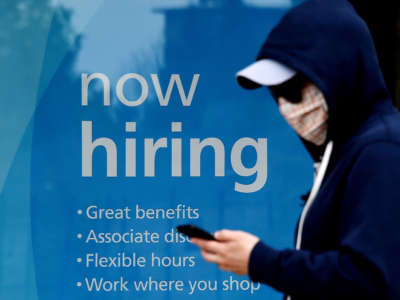 A man wearing a face mask walks past a sign "Now Hiring" in front of a store amid the coronavirus pandemic on May 14, 2020, in Arlington, Virginia.