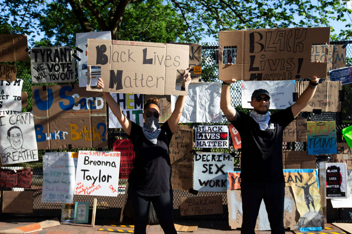 Protesters hold up signs near the White House's recently erected security fence, now turned into a memorial against police brutality and the death of George Floyd, during a peaceful protest on June 7, 2020, in Washington, D.C.
