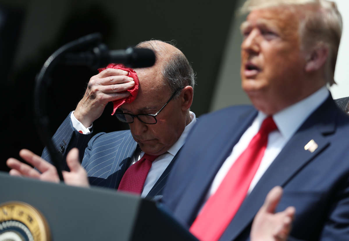 Larry Kudlow dabs sweat from his brow while standing beside trump