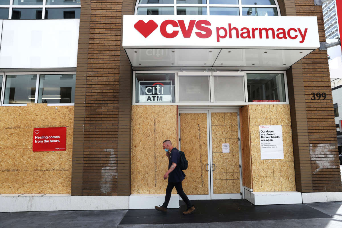 A man walks by a boarded-up cvs