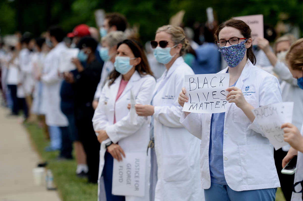 Medical professionals wearing ppe stand during a protest as one displays a sign reading "Black Lives Matter"