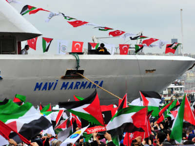 People wave Palestinian and Turkish flags in front of a ship reading "Mavi Marmara"