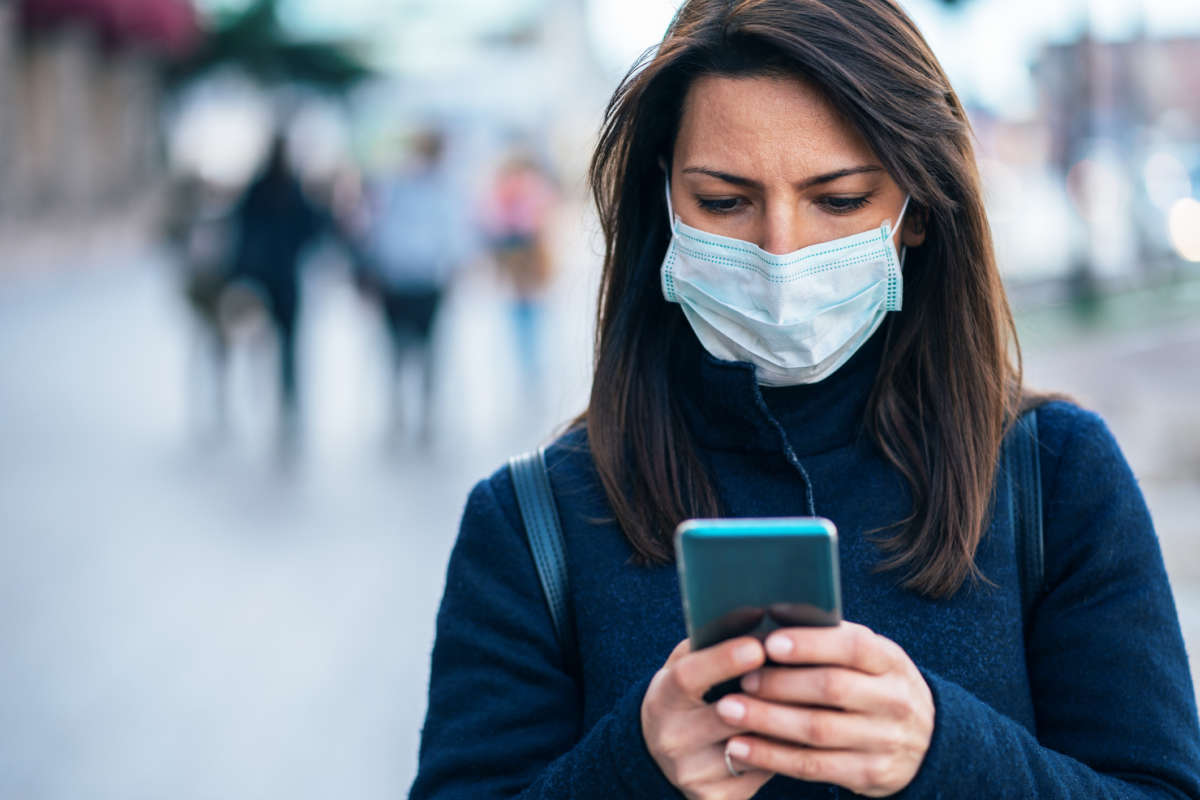 A woman looks at her phone while wearing a facemask outdoors