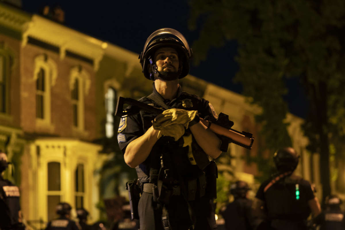 A cop holds a tear gas launcher like it's his own child