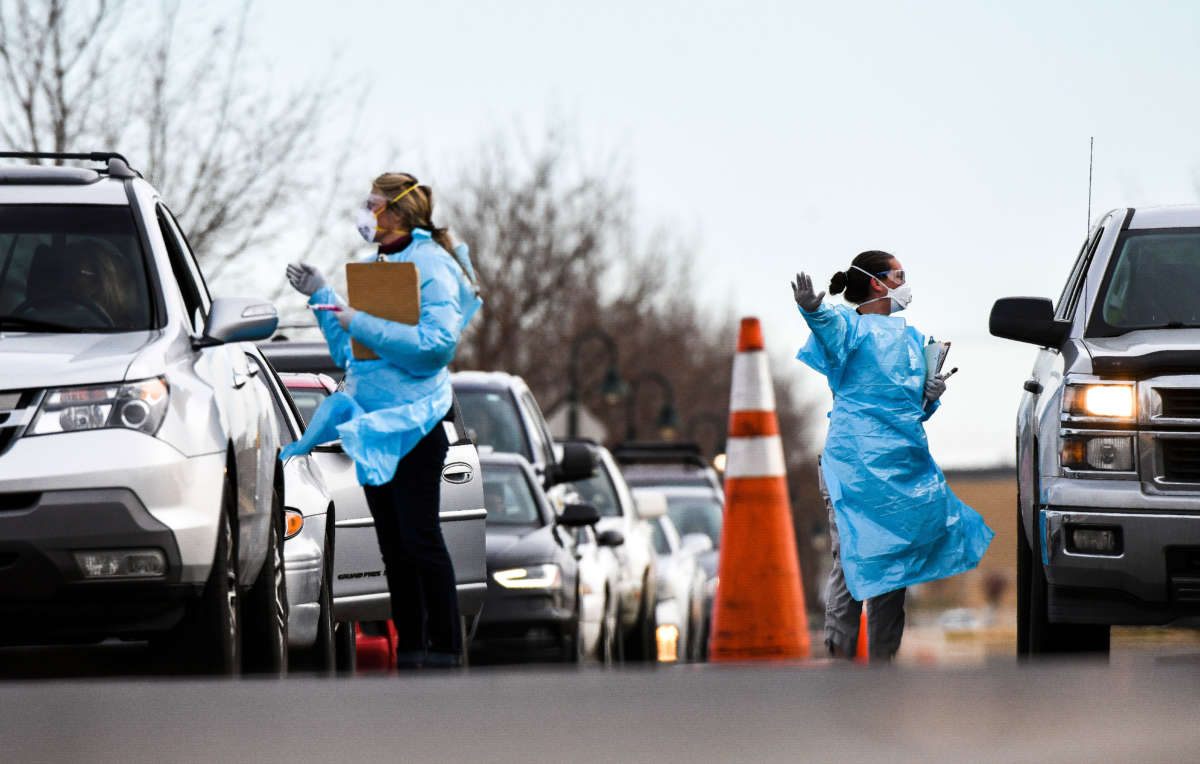 Health care workers from the Colorado Department of Public Health and Environment check in with people waiting to be tested for COVID-19 at the state's first drive-up testing center on March 12, 2020, in Denver, Colorado.