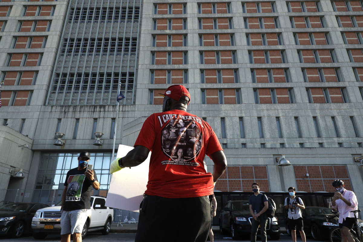 A man in a red shirt showing portraits of people slain by police holds a sign during a protest in front of a prison