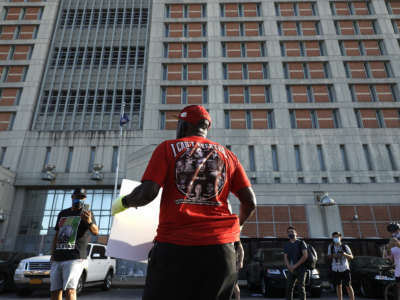 A man in a red shirt showing portraits of people slain by police holds a sign during a protest in front of a prison