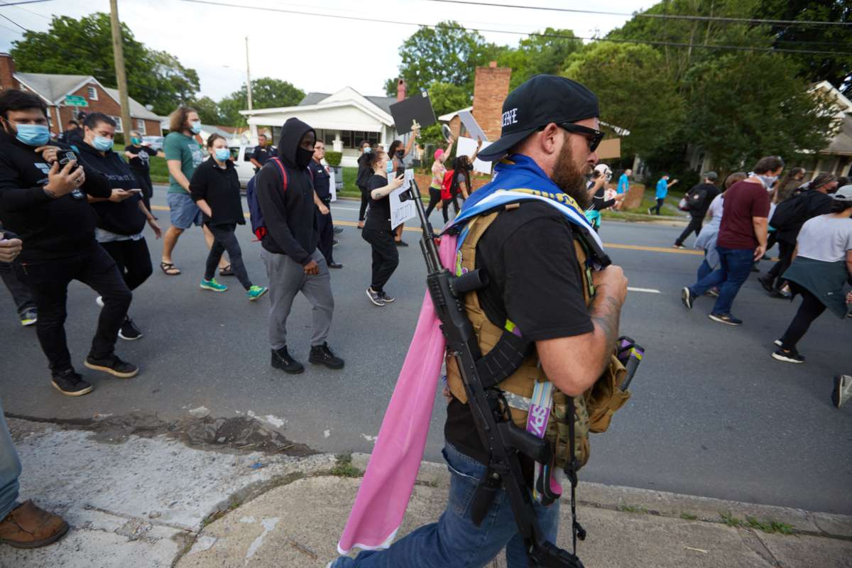 A member of the far-right militia, Boogaloo Bois, walks next to protestors demonstrating outside Charlotte-Mecklenburg Police Department Metro Division 2 just outside of downtown Charlotte, North Carolina, on May 29, 2020.