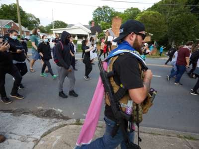 A member of the far-right militia, Boogaloo Bois, walks next to protestors demonstrating outside Charlotte-Mecklenburg Police Department Metro Division 2 just outside of downtown Charlotte, North Carolina, on May 29, 2020.