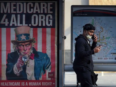 A pedestrian wearing a protective mask checks her phone near as she walks by a Medicare for All bus stop billboard in Washington, D.C., on June 3, 2020.