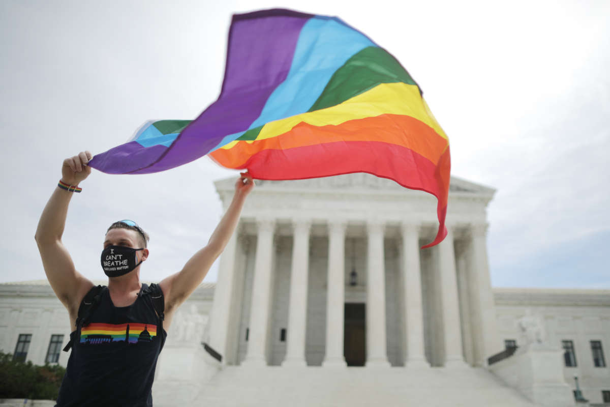 A man wearing an "I can't breathe" mask billows a rainbow flag on the steps of the supreme court