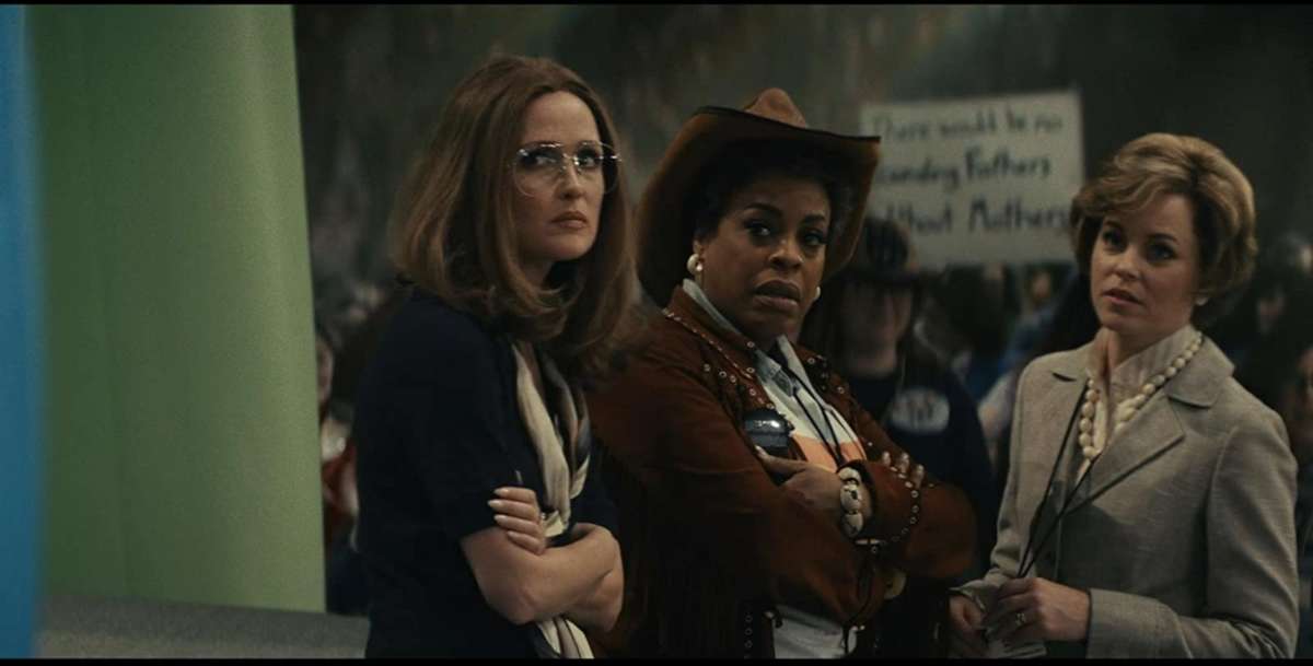 Three women in period garb from the U.S. 1970s stare in disgusted unison at something happening offscreen