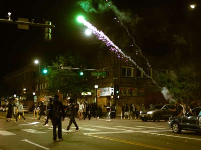 people walk in the street as fireworks are lit