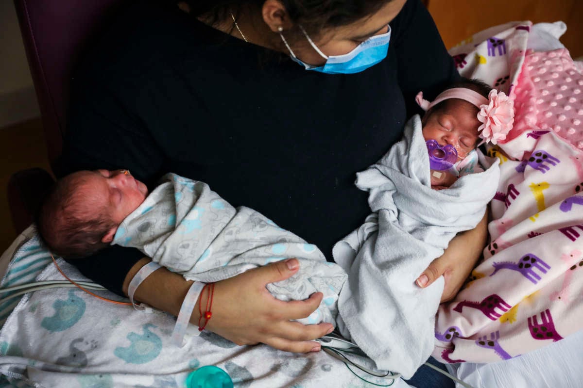 A mom cradles her two sleeping babies in her arms