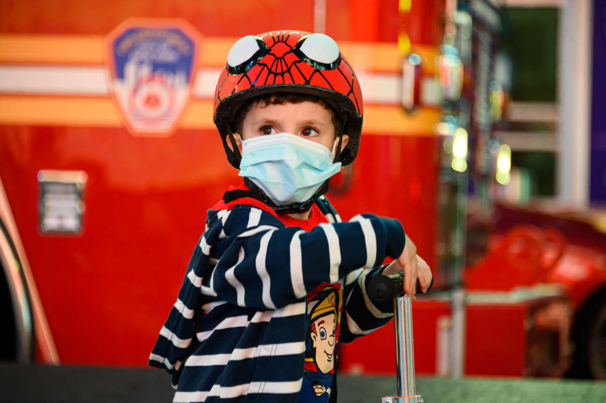 A child in a spiderman helmet and a face mask rides a bike
