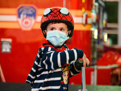 A child in a spiderman helmet and a face mask rides a bike