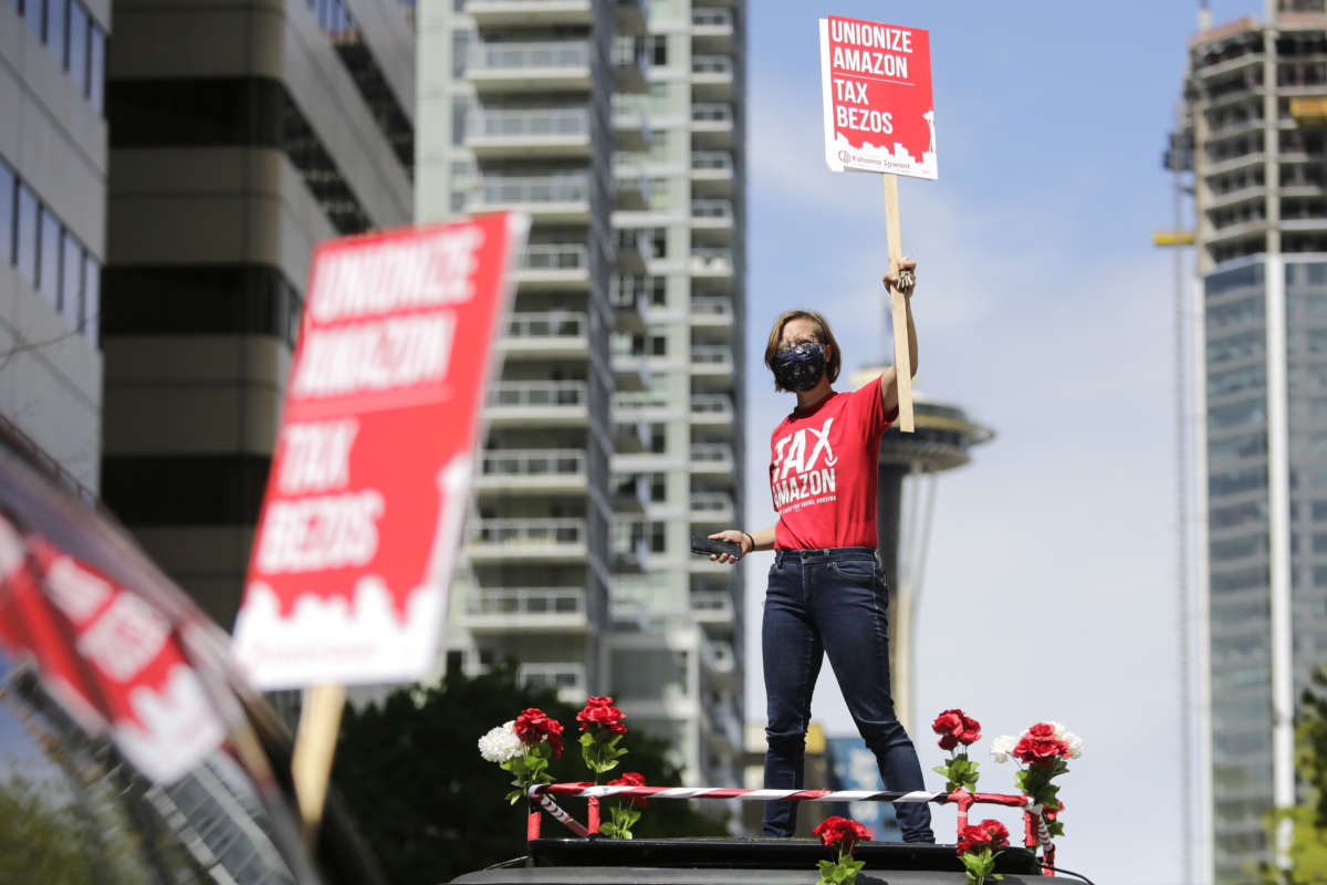A protester stands atop a car holding a sign reading "UNIONIZE AMAZON -- TAX BEZOS" during a protest blocking an intersection