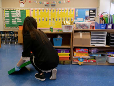 A teacher faces away from the camera while putting things on a shelf