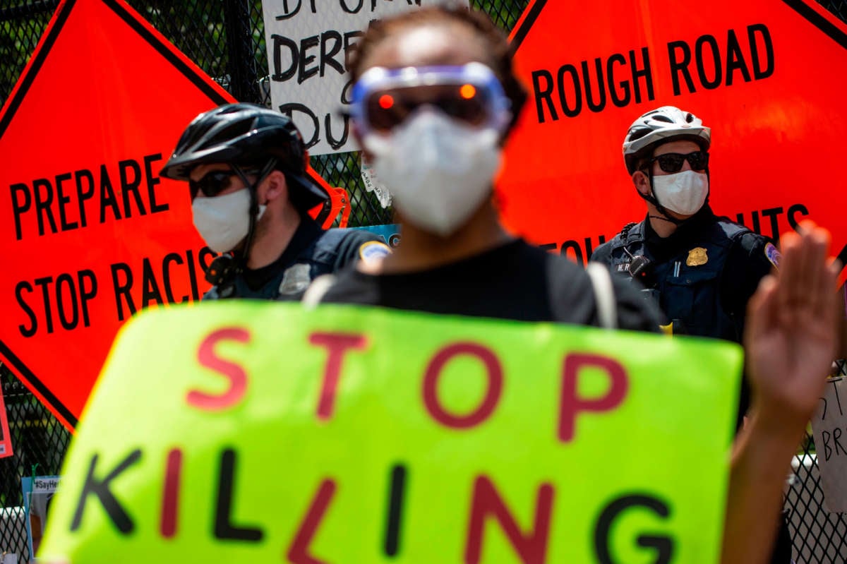 A protester holds a sign that reads "Stop Killing" while standing near policemen during a small standoff between police and protesters in front of Lafayette Square near the White House in Washington, D.C., on July 4, 2020.