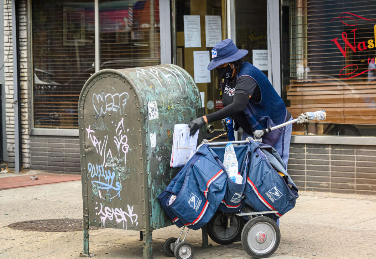 A usps worker collects mail from a graffiti-sprayed federal mailbox