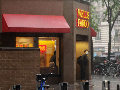 A person wearing a mask stands under a Wells Fargo awning in the rain on July 9, 2020, in New York City.